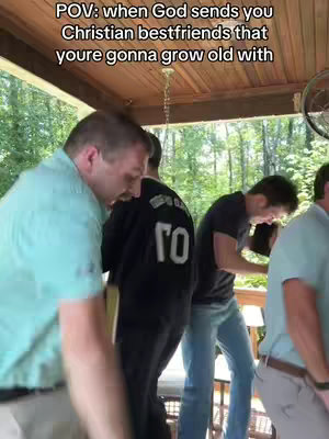 The image shows five men standing on a porch or deck, seen from the waist up. They appear to be casually interacting with each other, with the focus on their camaraderie. The background includes trees and a wooden ceiling.
