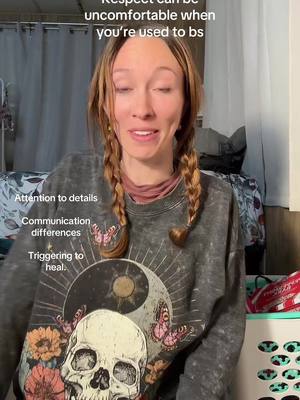 A woman with long, light brown hair in two braids is the central figure. She's wearing a gray sweatshirt with a graphic print featuring a skull, flowers, and a yin-yang symbol. Text overlays float near her; a bedroom setting is hinted at.