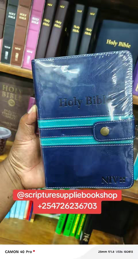 The cover image showcases a person holding a blue Holy Bible with a teal and white stripe. The Bible is in plastic wrap. Behind the main subject are shelves filled with more books, including various editions of the Bible in different colors. There's a red rectangle with white text in the image with contact details. The overall layout is well-lit and focuses on presenting the product.