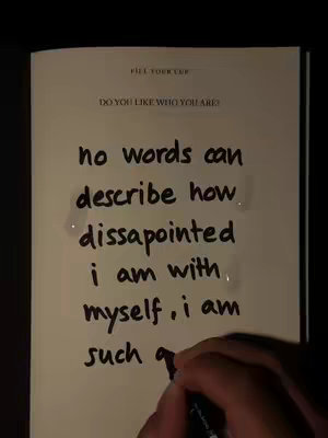 A hand writing on a light-colored page within a book, with the text filling the space. The page is lit from an angle, casting shadows where the pages curve.