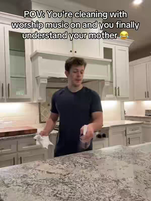 A man stands in a modern kitchen, wiping a countertop with a cloth. The setup suggests a POV shot, implying the viewer is also cleaning.