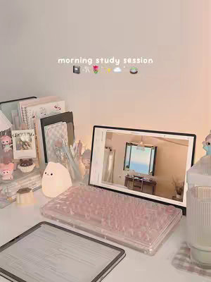 A serene, aesthetic image of a desk setup, likely for studying or work. A transparent keyboard cover on a laptop sits in the foreground, with an iPad visible below it. Various items such as books, stationery, and decorative figurines are arranged to create a clean and inviting workspace. The color palette is dominated by soft pastels, creating a cozy and motivating atmosphere.
