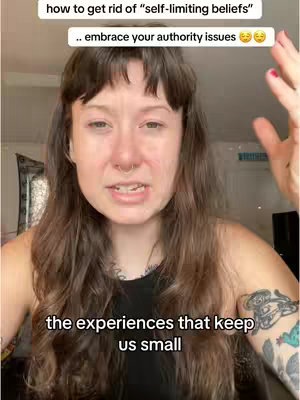 A woman with long, wavy brown hair is the central focus, with text overlays at the top and bottom. She has a neutral to slightly concerned facial expression, with a nose ring. Her arms are raised to the side with a partially visible tattoo on her arm.
