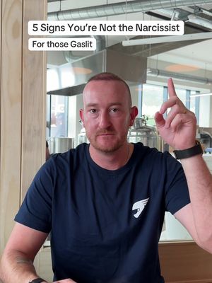 A man with short hair and a beard is centered in the shot, wearing a dark blue t-shirt. He looks directly at the camera with a serious expression and is pointing his right index finger upward. Text overlays the image at the top left.