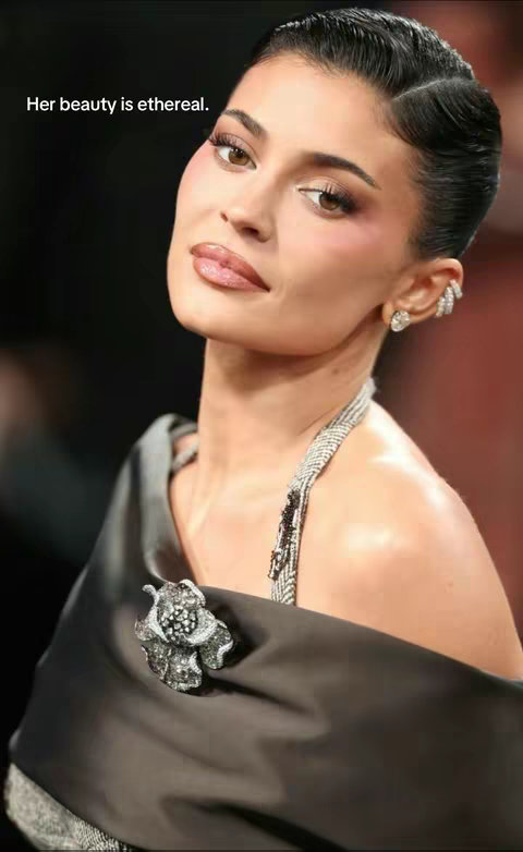 The cover image features a close-up of a woman's face, likely Kylie Jenner. She is facing slightly to the side with a subtle smile. Her face is adorned with professionally done makeup including highlighted blush and lip gloss. She is wearing a dark, off-the-shoulder dress with a shimmering necklace. Her hair is styled back, showing off a detailed ear cuff. The background is dark and blurred.