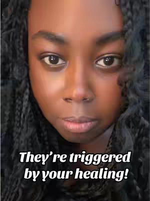 A close-up shot features a Black woman with long, dark, braided hair. She has brown eyes and a neutral expression. Text overlayed on the image reads, 'They're triggered by your healing!'