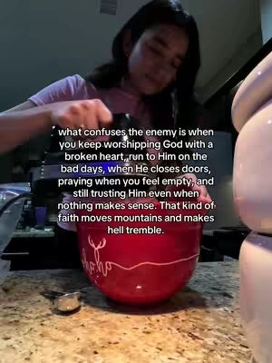 A person, likely a woman, is shown in a domestic kitchen setting. She is seen from the chest up, slightly angled towards the camera, with dark hair. The background features kitchen elements, including countertops and appliances. The central element is a large, red mixing bowl. Text overlays the image, with the woman wearing a pink shirt.