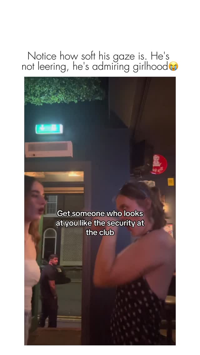 Two women are standing side-by-side, one facing the camera and the other turned away. Behind them is a doorway with a security guard visible in the background. Text is overlaid on the image.