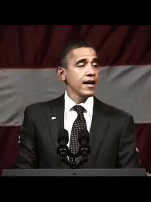 The image is of Barack Obama speaking at a podium, with a backdrop of the American flag. He is wearing a dark suit, a white shirt, and a patterned tie and he is positioned behind two microphones. The lighting appears to be from overhead, casting shadows and highlighting his face. The composition is formal and oriented for a speech or presentation.
