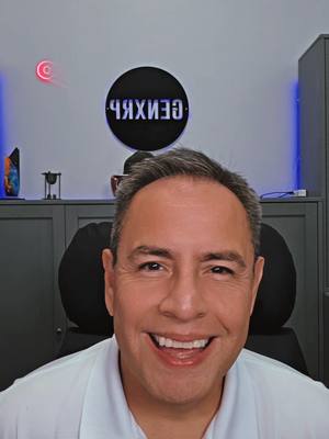 A man with short gray hair smiles widely at the camera. He's wearing a white polo shirt. Behind him is a room with a gray cabinet, a backlit circle with the name "ЧЯИХЗЭ" in reverse, and a red neon "c" shape on the wall.