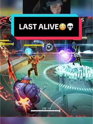 The image shows a gaming scene from a mobile game. The top portion features a facecam of the streamer. A large black and blue bar in the middle displays the words 'LAST ALIVE' along with an emoji. Below, a game environment unfolds. There are several characters engaged in combat: a player with a sword, a fiery-looking character, and a person with a glowing bow. The action appears dynamic, with brightly colored energy effects and health bars. The scene is viewed from an angled, overhead perspective.
