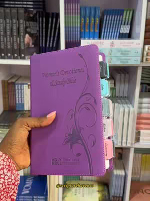 A hand holding a partially visible purple Bible open to the tabs. The spine of the Bible, the tabs, and the hand are in focus against the background.