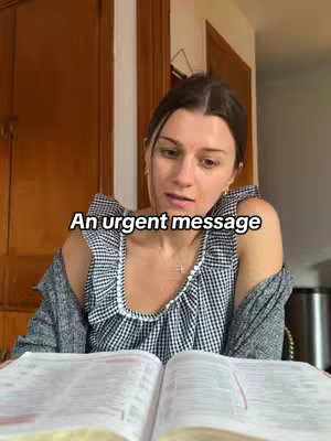 A woman is seated, facing forward and looking down. She's wearing a black-and-white gingham top, overlaid with a grey cardigan. The woman has dark hair, and is holding a Bible open in front of her, with the text overlayed that says 'An urgent message'. The background is a blurred interior lit by natural light through the door.