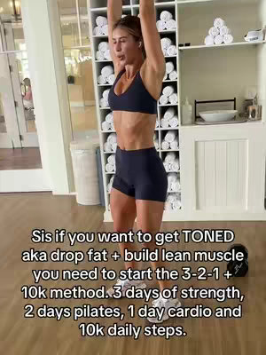 A woman is shown in athletic wear indoors, performing what appears to be an overhead strength exercise, possibly with dumbbells. She is in a well-lit gym setting with white shelving in the background. The image emphasizes fitness and strength training.