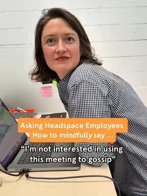 A woman with short dark hair leans towards a laptop in a well-lit office setting. She is wearing a checkered shirt and appears to be looking upwards with a slightly inquisitive expression. An orange rectangular box with white text overlays partially obscures the laptop and the rest of the room.