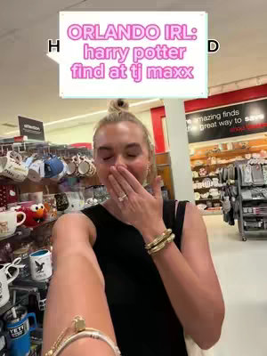 The image shows a woman holding her hand up to her mouth and appearing surprised or excited. She is in what appears to be a retail store, with shelves of Harry Potter merchandise in the background. A text overlay indicates that it is an "Orlando IRL: Harry Potter find at TJ Maxx"