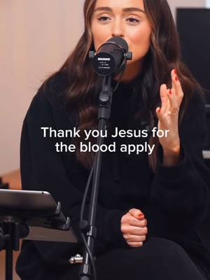 A woman is holding a microphone and looking up towards the sky in front of a dark background, seemingly presenting Christian worship music.