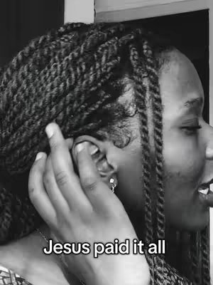 A black and white photo of a woman with braided hair. She is facing right, with her left hand near her ear. The text overlay states, 'Jesus paid it all'.