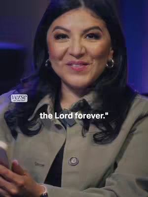 A woman with dark hair and wearing a light jacket is seen smiling slightly and looking toward the viewer. Text is overlaid at the bottom, and a logo is displayed in the top-left corner.