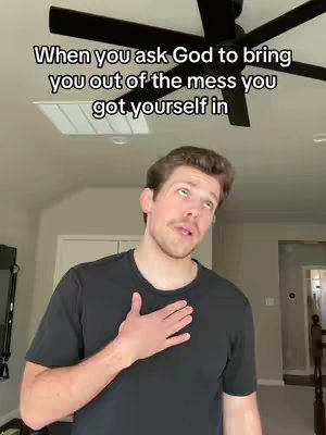 A man with light skin stands slightly off-center, facing upwards with a hand on his chest, wearing a dark t-shirt. He is in a room with a light-colored ceiling, a partially visible ceiling fan, and window accents. Gray text is displayed in the upper part of the image.