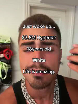 A selfie-style video cover image featuring a young man in a dark top, a silver chain necklace, and text overlaying his face. The background is a blurred room with light-colored walls. There is text overlayed on the video.
