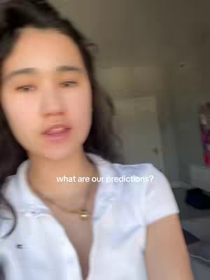 A young woman with dark hair and pale skin, wearing a white polo shirt and a gold necklace, is centered in the frame, filling most of the space with the upper half of her body. The background is blurred, showing what appears to be a room with a window. The image has warm lighting and a casual feel, with a text overlay at the bottom that reads 'what are our predictions?'