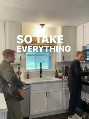A kitchen scene with a man playing guitar and a woman standing near stove. Text overlayed on the image reads "SO TAKE EVERYTHING NOT".