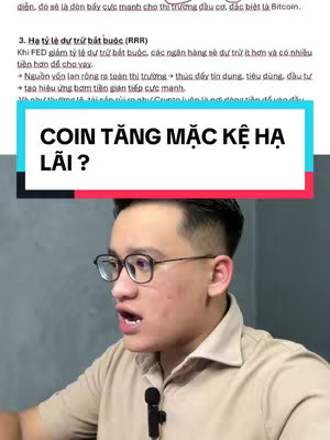 A man in a beige shirt and glasses is talking, with a microphone attached. Overlaid on the image is a text box in pink and turquoise that says “COIN TĂNG MẶC KỆ HẠ LÃI?”
