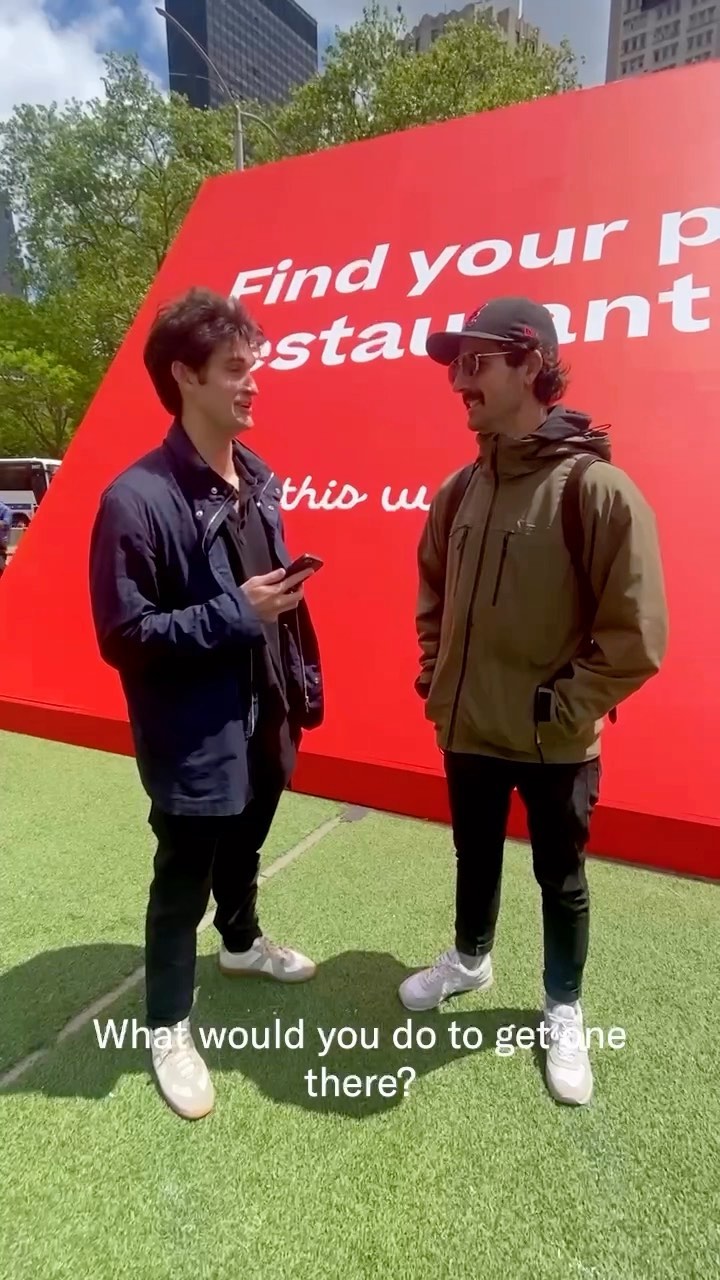 Two men are standing on artificial turf with a large red sign in the background that says the text "Find your restaurant". Text overlay in the bottom of the image reads "What would you do to get one there?"