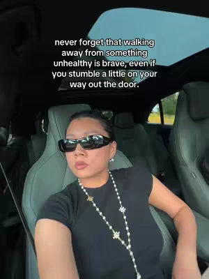 A woman wearing sunglasses and jewelry is seated in a car, looking at the camera with a serious expression. Text overlays the image.