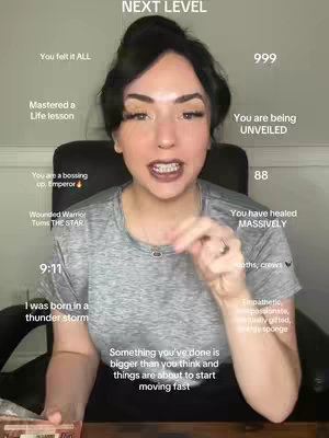 A woman with long dark hair is centered in the frame, looking directly at the camera with a slight smile. She is wearing a light gray t-shirt and has visible eye makeup and lip color. Various text overlays are scattered around her, including phrases like "NEXT LEVEL," "You felt it ALL," and numbers such as "999" and "88." The background is blurred, suggesting an indoor setting.