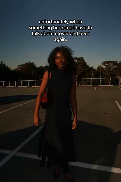 A woman in a black dress stands in a parking garage, facing the camera with a serious expression. Above her, text overlays describe her experience. The lighting is subdued, and the background suggests a late afternoon.
