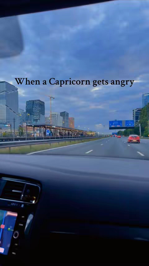 The cover image shows a view from inside a car, looking out onto a highway and a cityscape. The sky is overcast with hues of blue and grey. The foreground features the car's dashboard. In the mid-ground, a highway with several lanes of traffic, including a couple of red cars. In the background, there are modern buildings with glass facades, indicating an urban setting. Text overlayed on the image reads, "When a Capricorn gets angry".