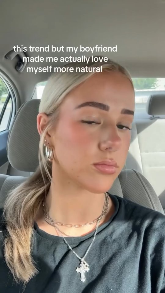 The cover image is a selfie of a young woman sitting in a car. She has blonde hair pulled back into a ponytail, large hoop earrings, and wears a black t-shirt with layered necklaces. The background is a blurred car interior; text overlayed along the top conveys a message about self-love and a boyfriend's influence. The lighting is soft, highlighting her features.