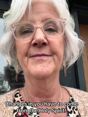 A close-up of a woman with short, wavy gray hair, wearing glasses and a patterned top, looking towards the camera with a slight smile. Text is overlaid at the bottom.
