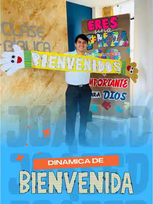 A man in a white shirt and dark pants stands in front of a banner. He is holding a yellow banner-like sign that says 'BIENVENIDOS' with a hand on the left side and a small bear-like figure on the right. The backdrop behind him includes a sign that says 'CLASE BIBLICA' The overall image has a bright, inviting feel.