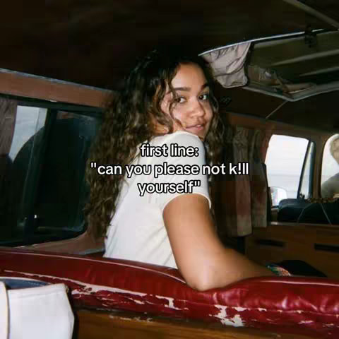 A young woman with long curly hair is shown inside what appears to be a vehicle. She is looking over her shoulder with a slight smile. The background is blurry with the interior of a vehicle visible.