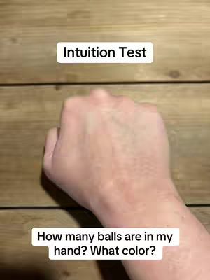 A first-person perspective shot showcasing a hand against a wooden background. The hand is making a fist. There are two text overlays: one at the top reading 'Intuition Test,' and another at the bottom asking, 'How many balls are in my hand? What color?'