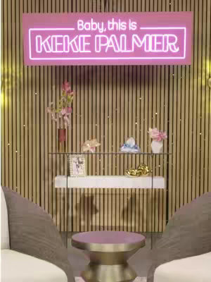 The cover image shows a pink neon sign that reads 'Baby, this is Keke Palmer'. Below the sign, there's a display shelf with decorative items like vases with flowers, and small objects. The background has a wooden panel design. There is a table and chairs in the foreground.
