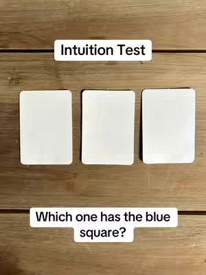 A wooden surface with three white rectangular cards and two text boxes. The top text box reads "Intuition Test", while the bottom box asks "Which one has the blue square?"