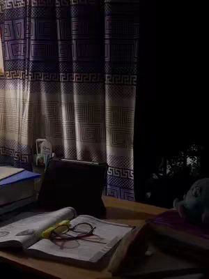 The image shows a desk in a dimly lit room. On the desk are textbooks, open notebooks, glasses, and a tablet covered with a black case. The background includes a patterned curtain and a dark area, possibly a window or wall. The overall tone is calm, suggesting a study or work environment.