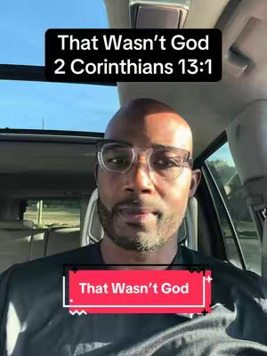 A man of color wearing glasses is seated in a car, presumably the driver's seat, and looking at the camera. Overlay text at the top reads 'That Wasn't God 2 Corinthians 13:1'. A secondary text box at the bottom shows 'That Wasn't God'. The background is a sunny day with blue skies visible through the sunroof. The man is wearing a black shirt and has a partial beard with a clear view of the seat and rearview mirror.