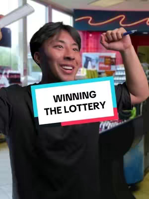 A man with dark hair is shown smiling broadly, seemingly celebrating. He has his arms raised, holding a pen in one hand and what appears to be a lottery ticket or paper in the other. The background hints at a convenience store setting, with shelves and product displays visible behind him. The image is bright with a focus on the man and his apparent excitement.