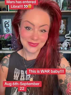 A woman with red hair and heavy makeup is centered in the frame. She smiles with red lips and blush, and red text overlays in different boxes are visible. The background includes a room, but is out of focus.