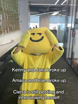 The image shows a person in a complete, bright yellow dog costume with a smiling face on the head. The costume covers the body and head, with arms visible at the sides. The person is in an office environment, the background indicating a casual workspace. Text overlays in a plain white font are added to the image explaining a sequence of breakups.