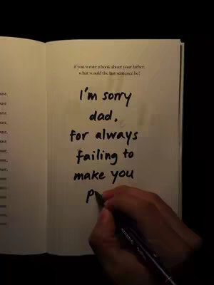 An open book on a dark surface. The left page contains some text, and the right page has the beginning of a handwritten apology letter. The hand of the person holding the pen is visible.