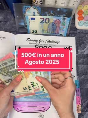 A woman's hands are shown holding and sorting through various Euro banknotes in front of an open notebook. The notebook features a "Saving Jar" challenge illustration, with a bold, red rectangular overlay that reads "500€ in un anno Agosto 2025". Various tabs are on the right side of the notebook. The background shows a clear plastic display with a 20 Euro note.