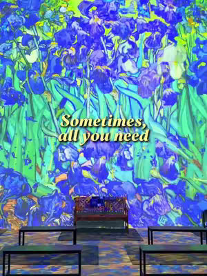 The image shows a digital art scene, possibly from a museum exhibit, featuring a vibrant floral backdrop of blue irises and green foliage. In the foreground, there's a decorative bench, and two black benches placed at eye level.