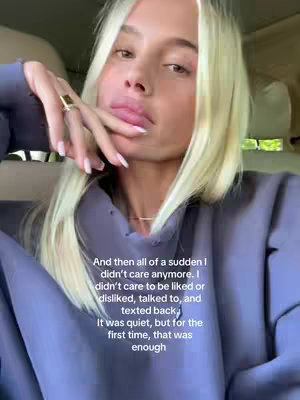 A woman with blonde hair and a purple sweater is holding her hand up to her mouth in a gesture of thought or contemplation. The background is blurred, suggesting she is in a car. Text overlayed on the image says, “And then all of a sudden I didn’t care anymore. I didn’t care to be liked or disliked, talked to, and texted back; It was quiet, but for the first time, that was enough”.