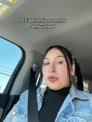 A woman is seated inside a car, facing the camera. She has dark hair pulled back, wearing a black top and a light blue denim jacket. The background shows the car's interior and a view of the outdoors. Text overlayed on the image reads: 'ICE detention center ambushed'.
